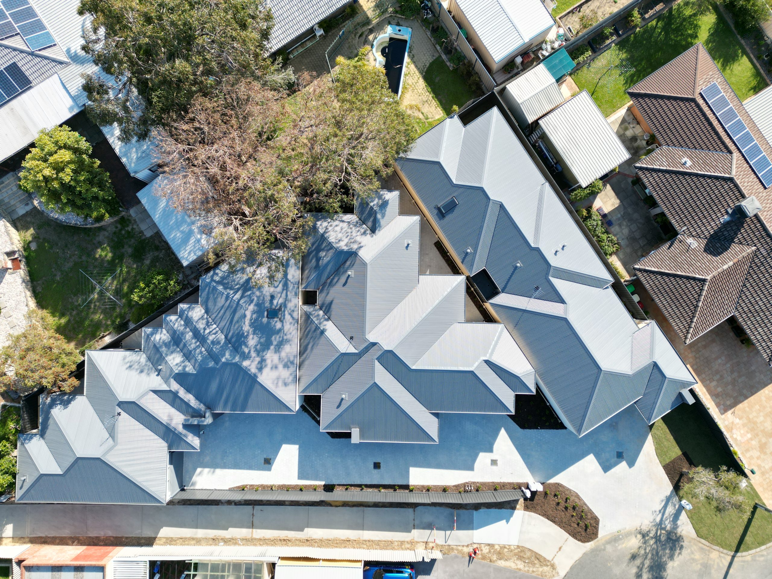 Aerial view of a Perth triplex development showcasing three modern dwellings with grey roofs, set on a subdivided block. The layout highlights efficient land use and stylish design, with ample driveway space and surrounding landscaping, illustrating an optimal use of residential property.